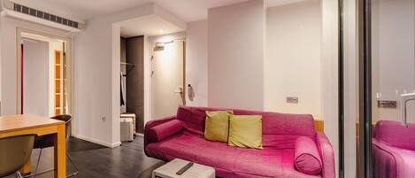 Una sala de estar moderna con una mesa de madera, un sofá rosa con cojines y una pequeña mesita blanca con un control remoto.