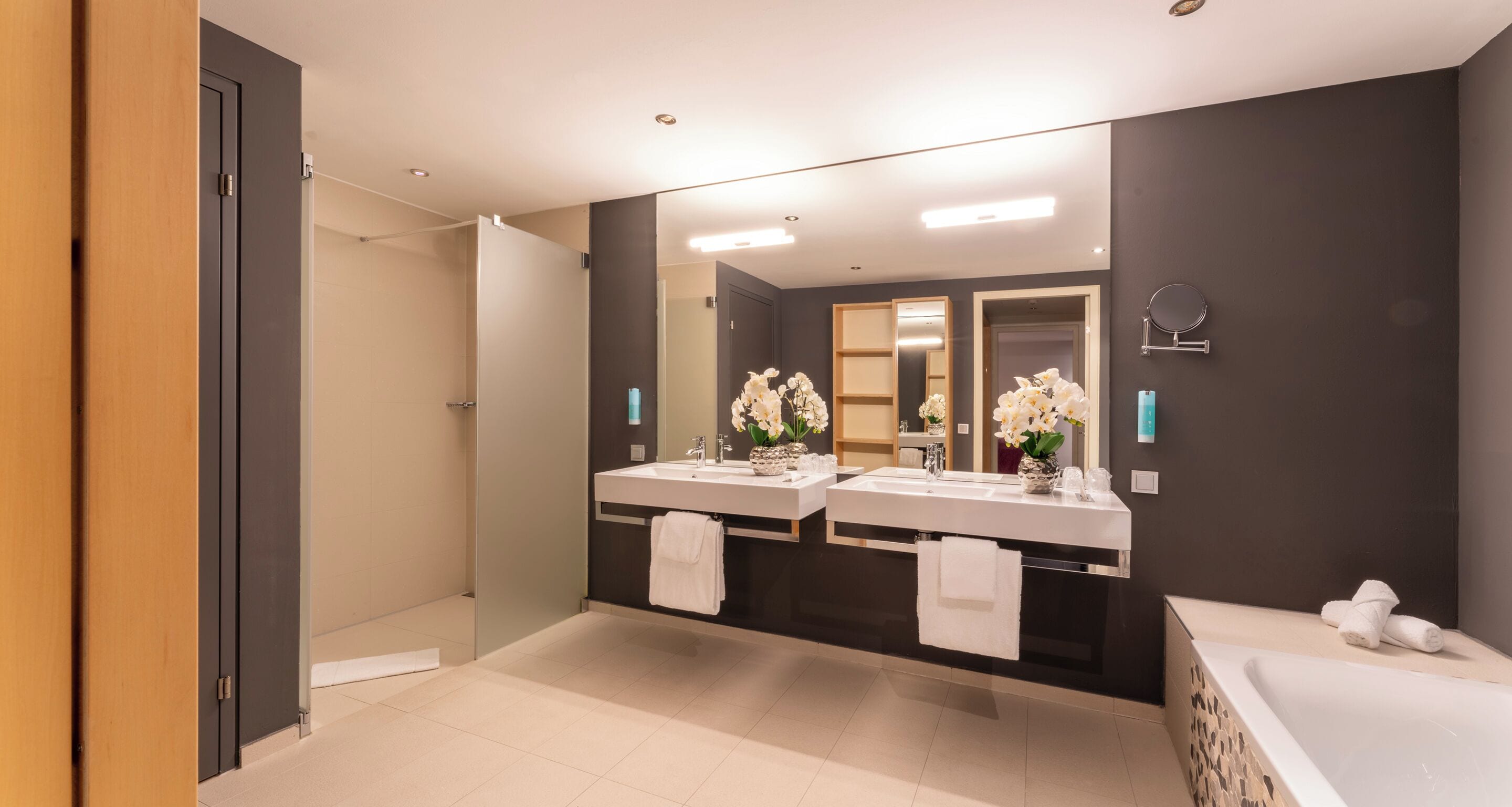 A modern bathroom with two sinks, a large mirror, and a bathtub.