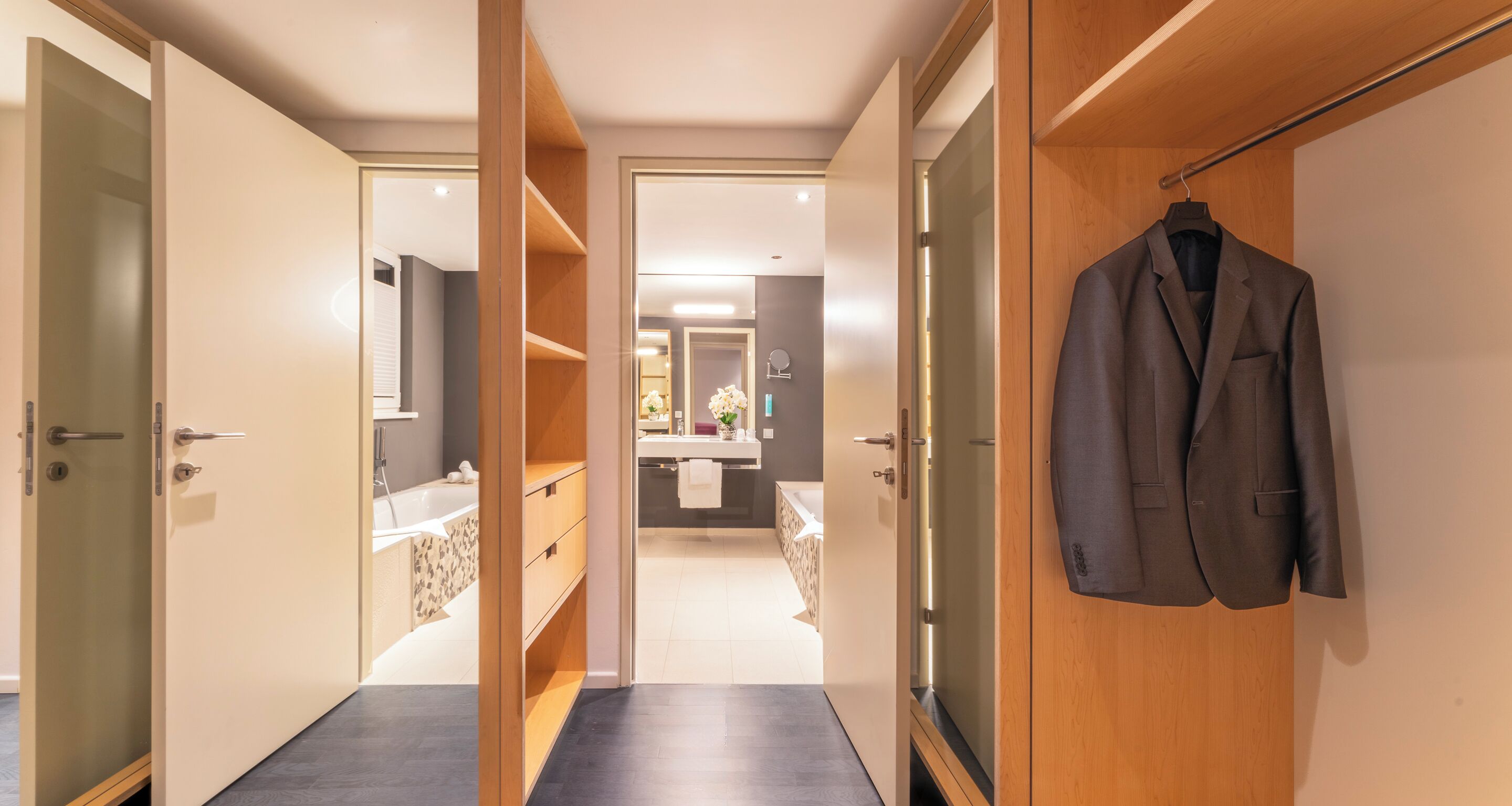 Una habitación de hotel con vestidor, baño con bañera y espejo.