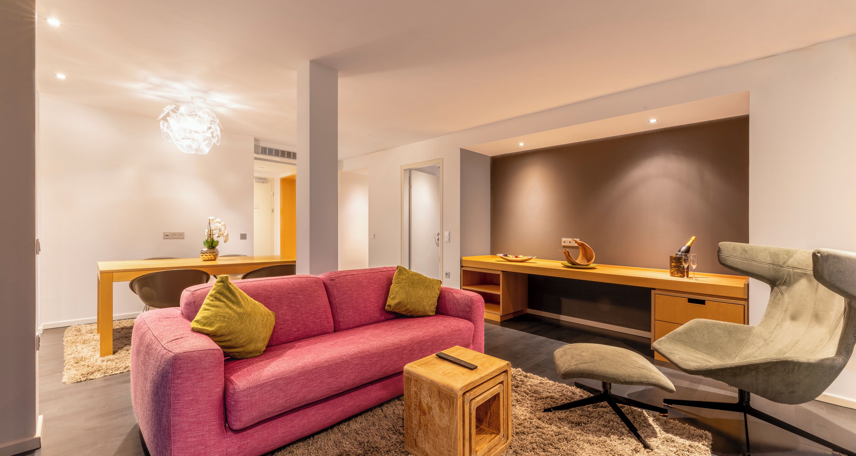 Ein modernes Wohnzimmer mit einem rosafarbenen Sofa, einem Holztisch und einem grünen Sessel.