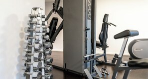 Un gimnasio con un soporte para mancuernas en la pared, una bicicleta estática y una cinta de correr.