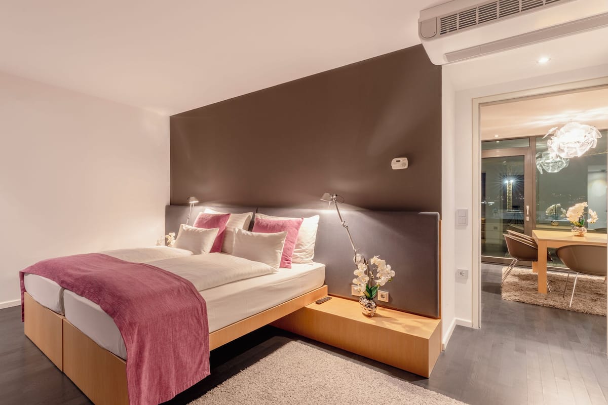 A modern bedroom with a bed, bedside table, and a view of the city at night.