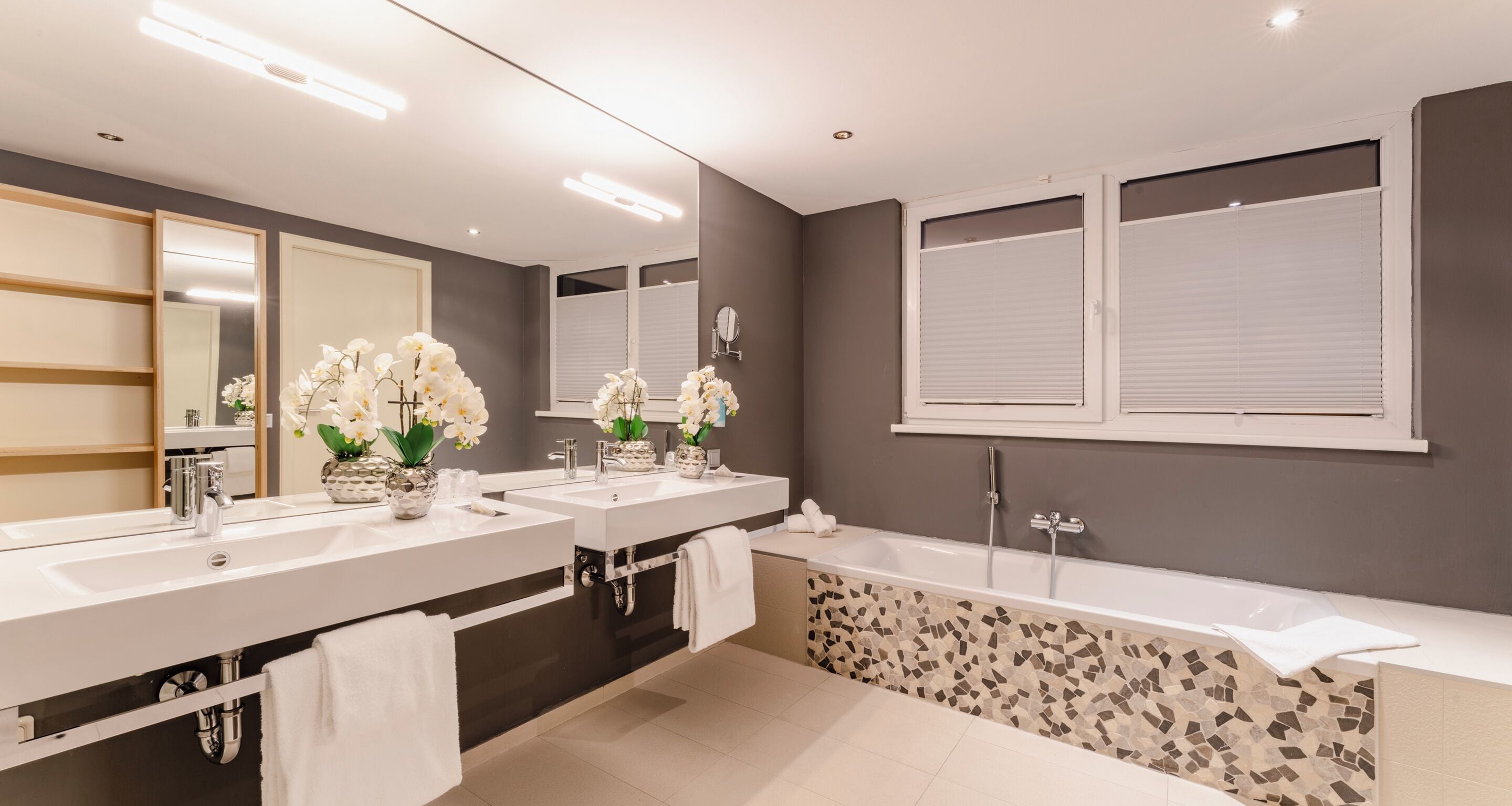 A modern bathroom with two sinks, a large mirror, and a bathtub.
