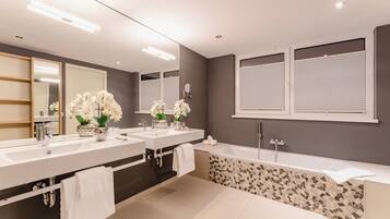 A modern bathroom with two sinks, a large mirror, and a bathtub.