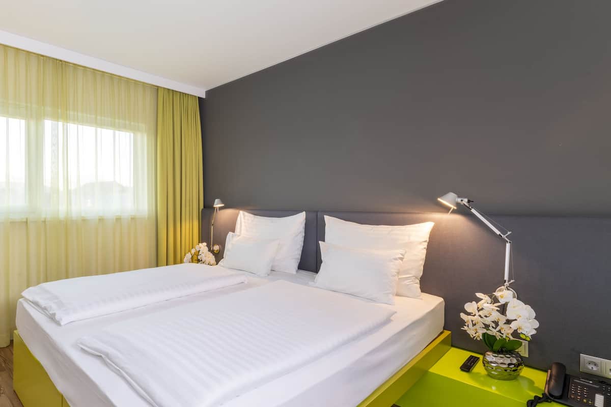 A hotel room with a bed, a nightstand with a lamp, a vase with flowers, and a telephone.