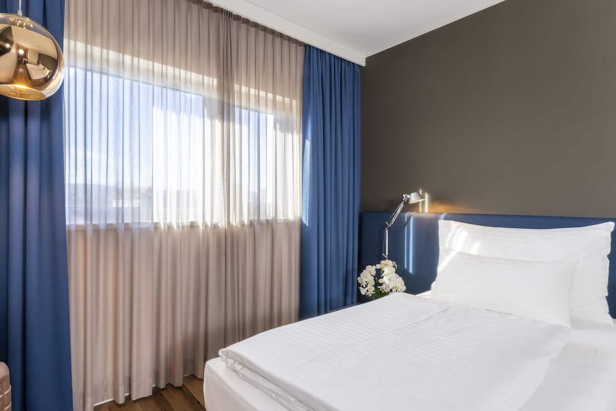 A hotel room with a bed, curtains, a bedside lamp, and a suitcase.