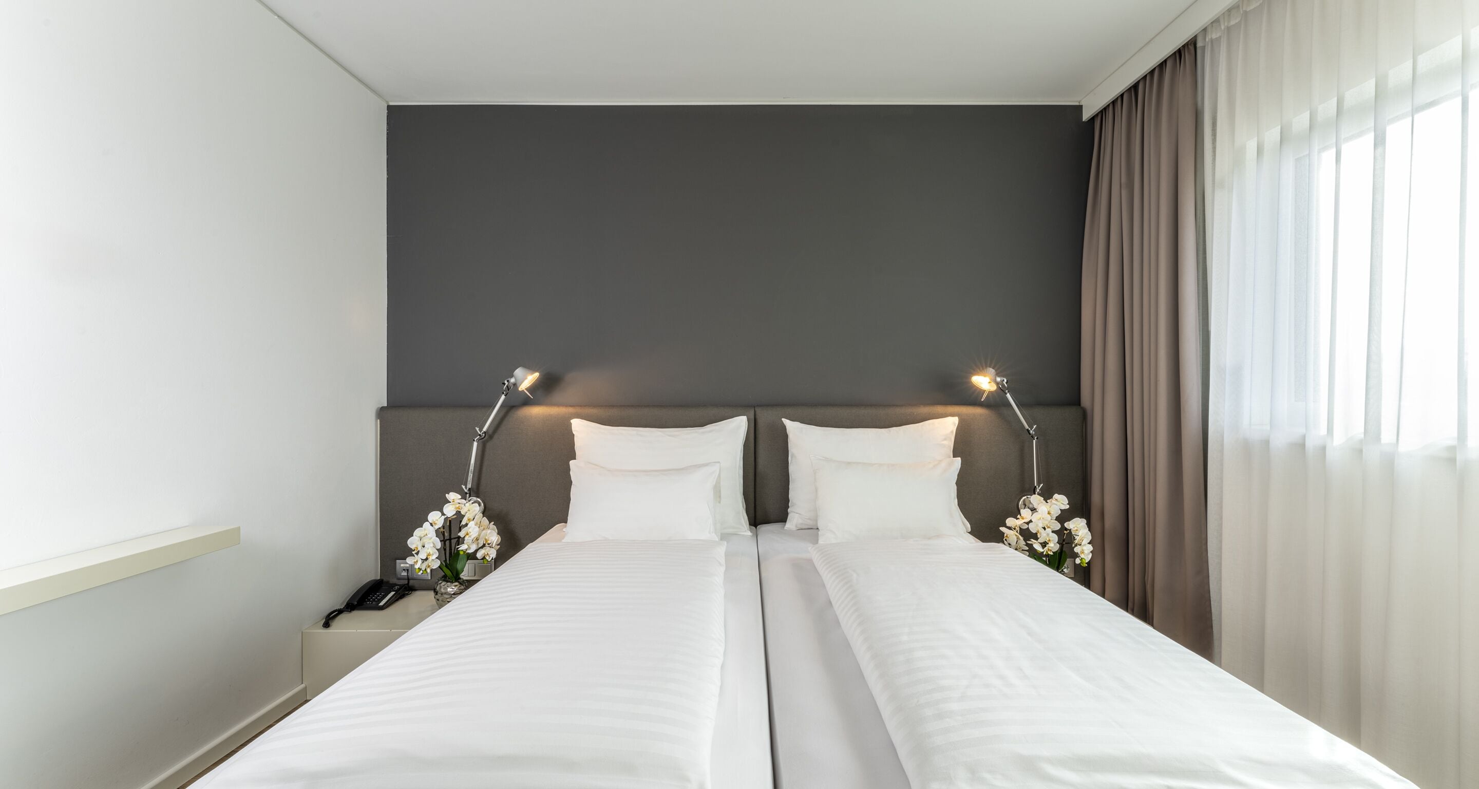 A hotel room with two beds, a nightstand with a phone, and a vase of flowers.