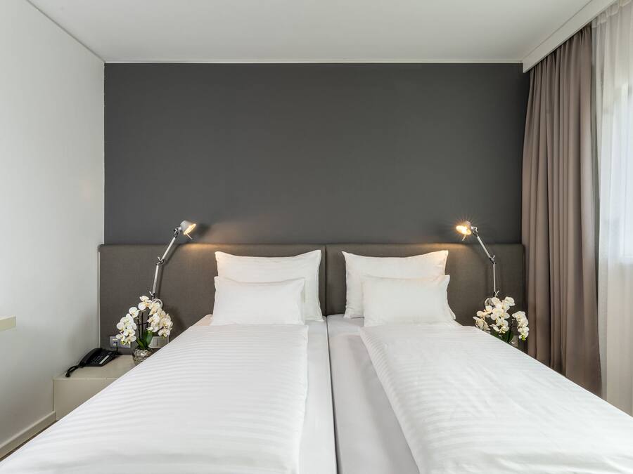 Hotellihuone, jossa on kaksi sänkyä, yöpöytä, jossa on puhelin, ja maljakko täynnä kukkia.