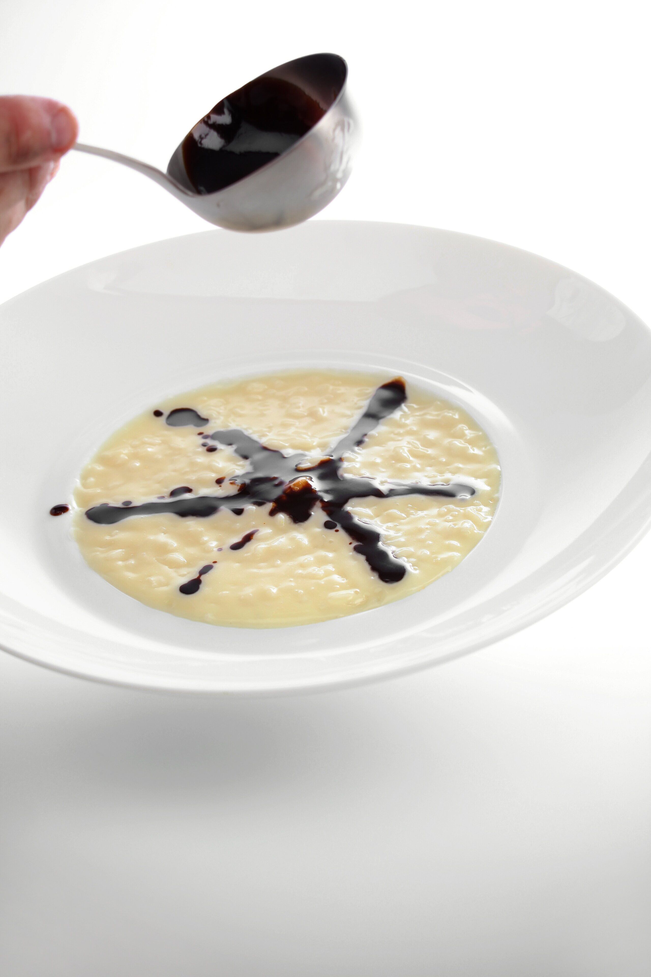 A white bowl with a spoonful of creamy food and dark sauce on a white background.