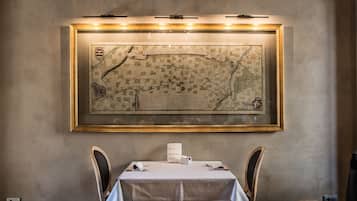 Un coin repas avec une table dressée pour deux personnes, une carte encadrée accrochée au mur et un menu posé sur la table.