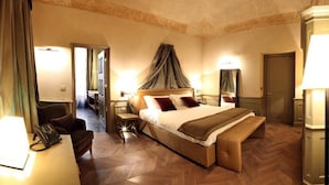 A hotel room with a large bed, bedside tables, a bench, a desk with a telephone, and a mirror. - Palazzo Righini (Fossano)