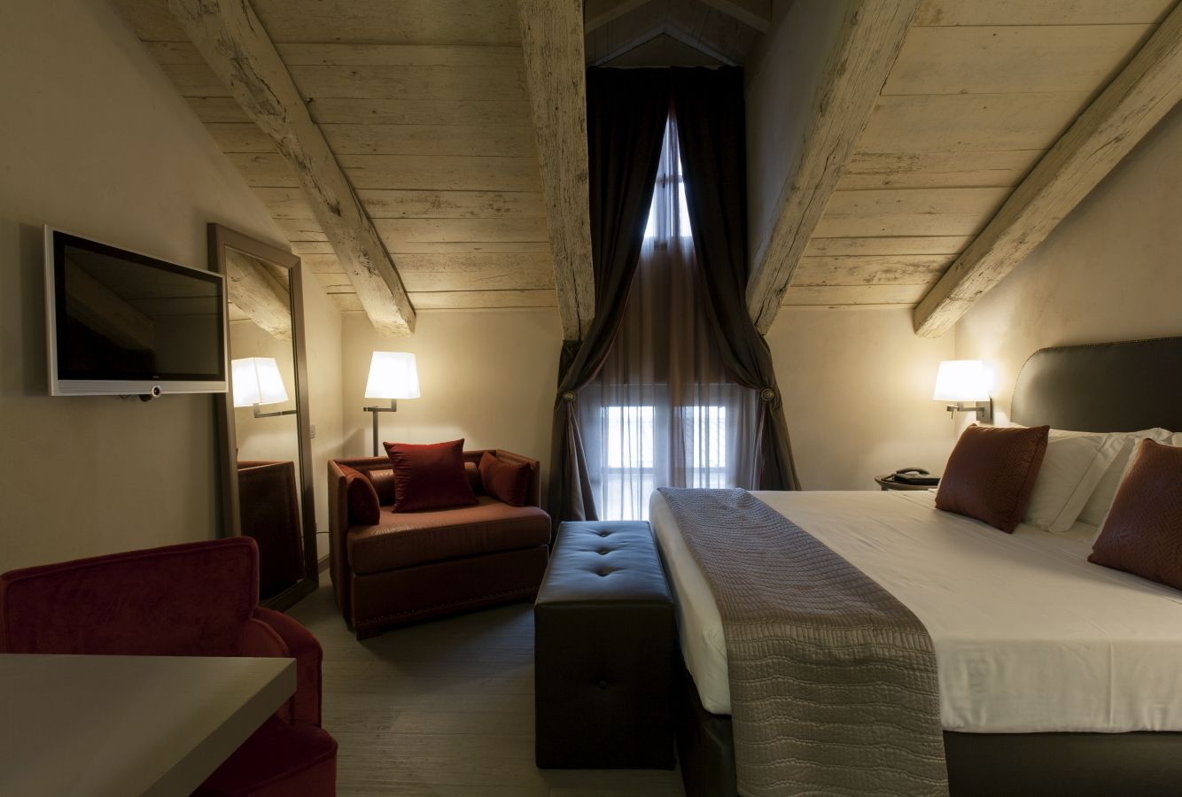 Habitación de hotel con una cama, un sofá rojo, una mesita, un televisor y una ventana con cortinas.