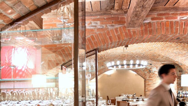 A restaurant with brick arches, wooden beams, and a glass display of wine glasses. - Palazzo Righini (Fossano)