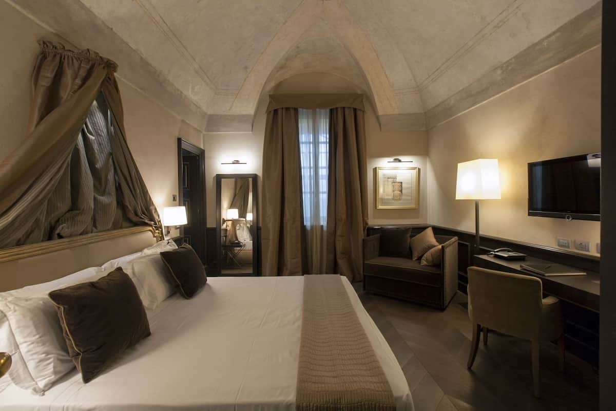 Quarto de hotel com uma cama grande, uma escrivaninha, uma cadeira, uma televisão e um espelho.