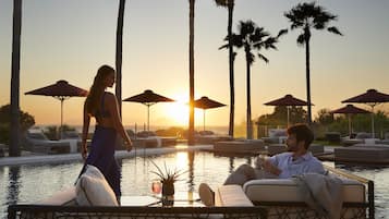 A poolside area with lounge chairs and umbrellas, a woman walking by, and a man relaxing with a drink.