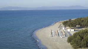 A beach with rows of sunbeds and umbrellas, a sandy shore, and a view of the sea and distant mountains.