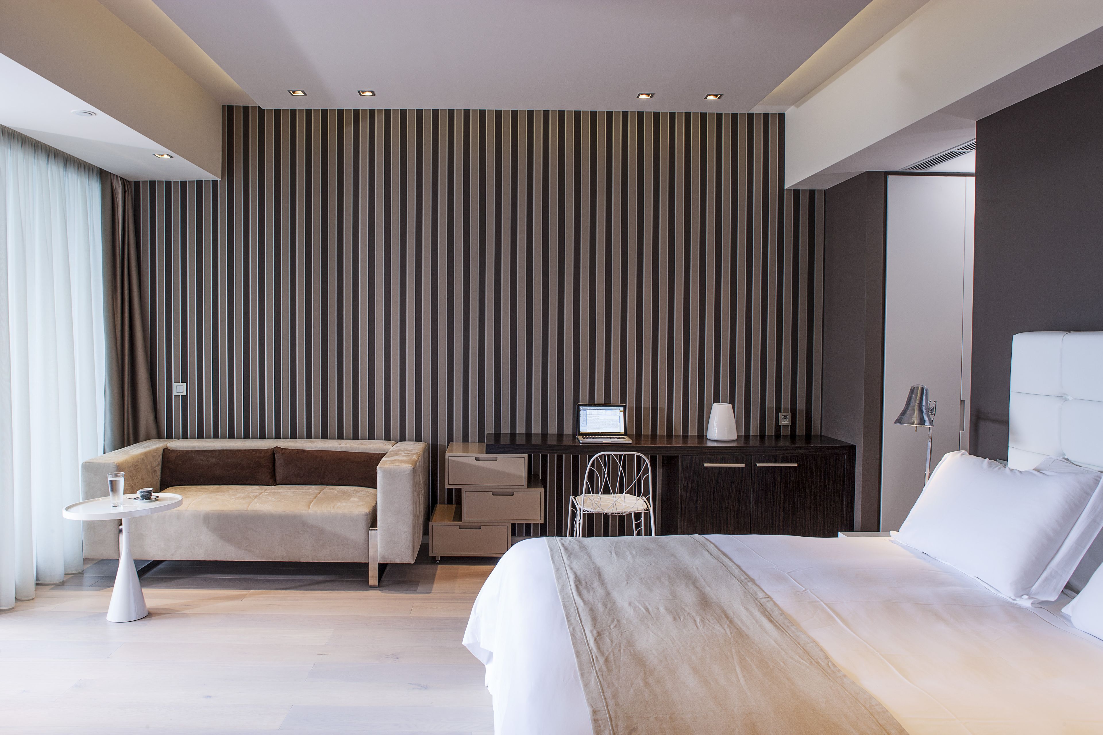 Una habitación de hotel moderna con una cama grande, un sofá, un escritorio con una computadora portátil y una silla.