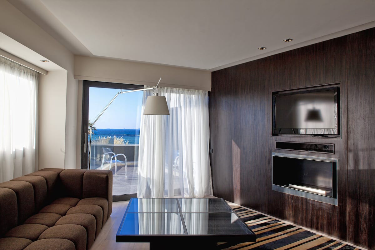 Een moderne woonkamer met een bank, een glazen salontafel, een televisie en uitzicht op de oceaan door een groot raam.