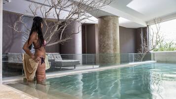 A modern indoor pool with clear water, a glass balustrade, and a lounge area with a sofa.