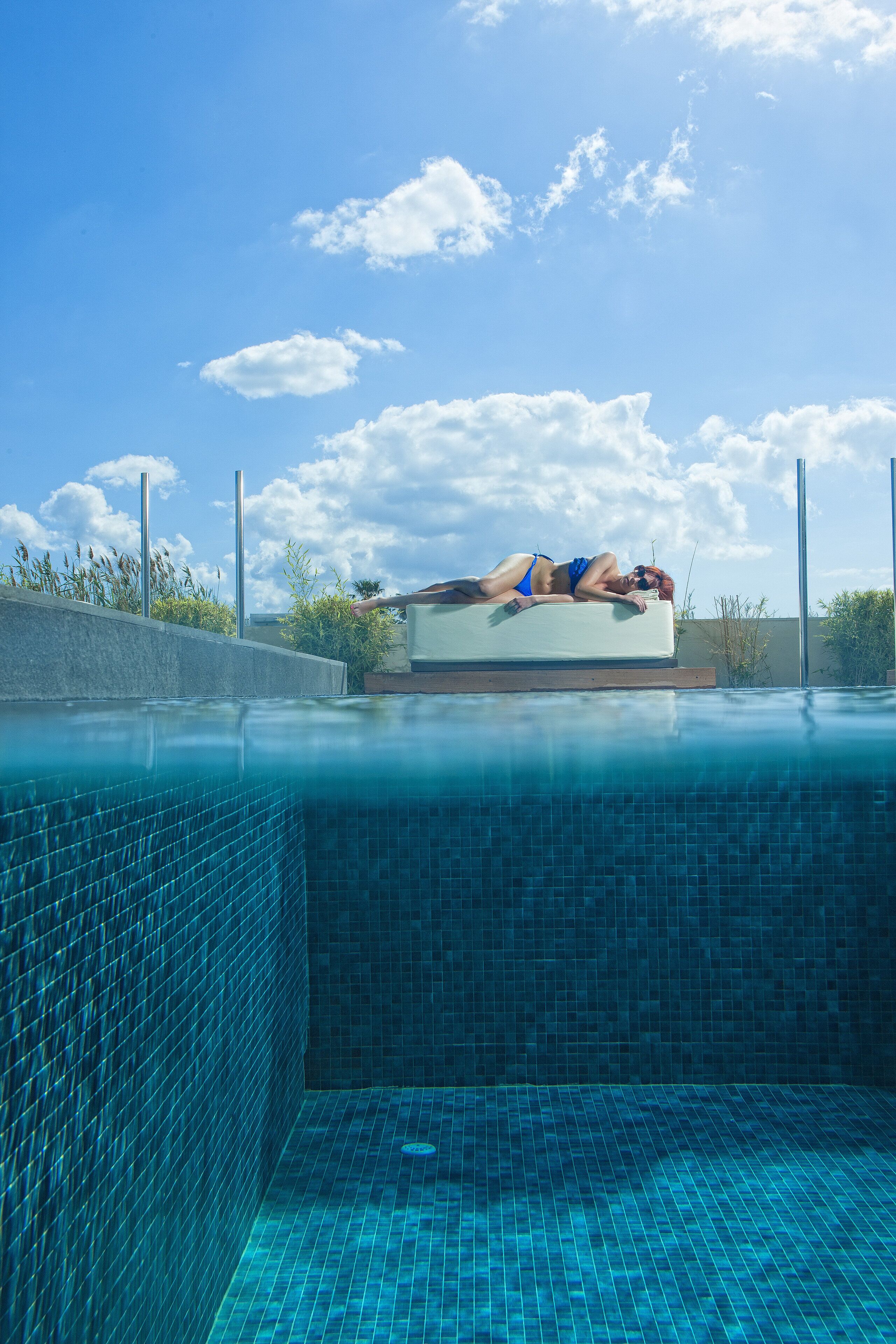A person lying on a floating platform in a clear blue pool with tiled walls.