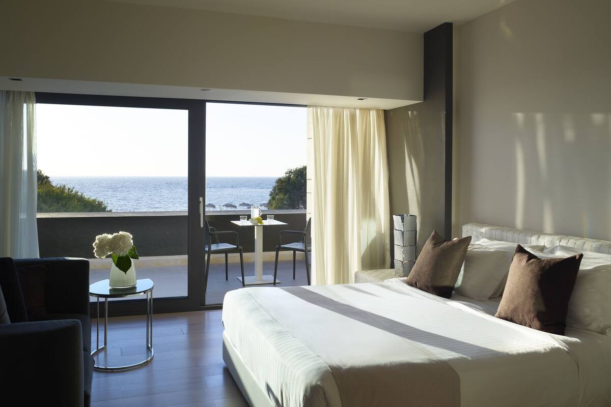 Hotelkamer met een groot bed, een klein tafeltje met stoelen, uitzicht op zee en een balkon.
