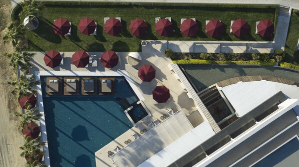 Luchtbeeld van een hotel met een zwembad, buitenmeubilair met parasols en een aangelegde tuin.