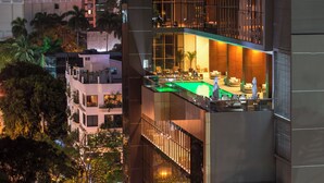 Un edificio moderno con zona de lounge en la azotea, ventanas amplias y un balcón con vistas a la ciudad.