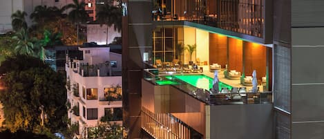 Un edificio moderno con zona de lounge en la azotea, ventanas amplias y un balcón con vistas a la ciudad.