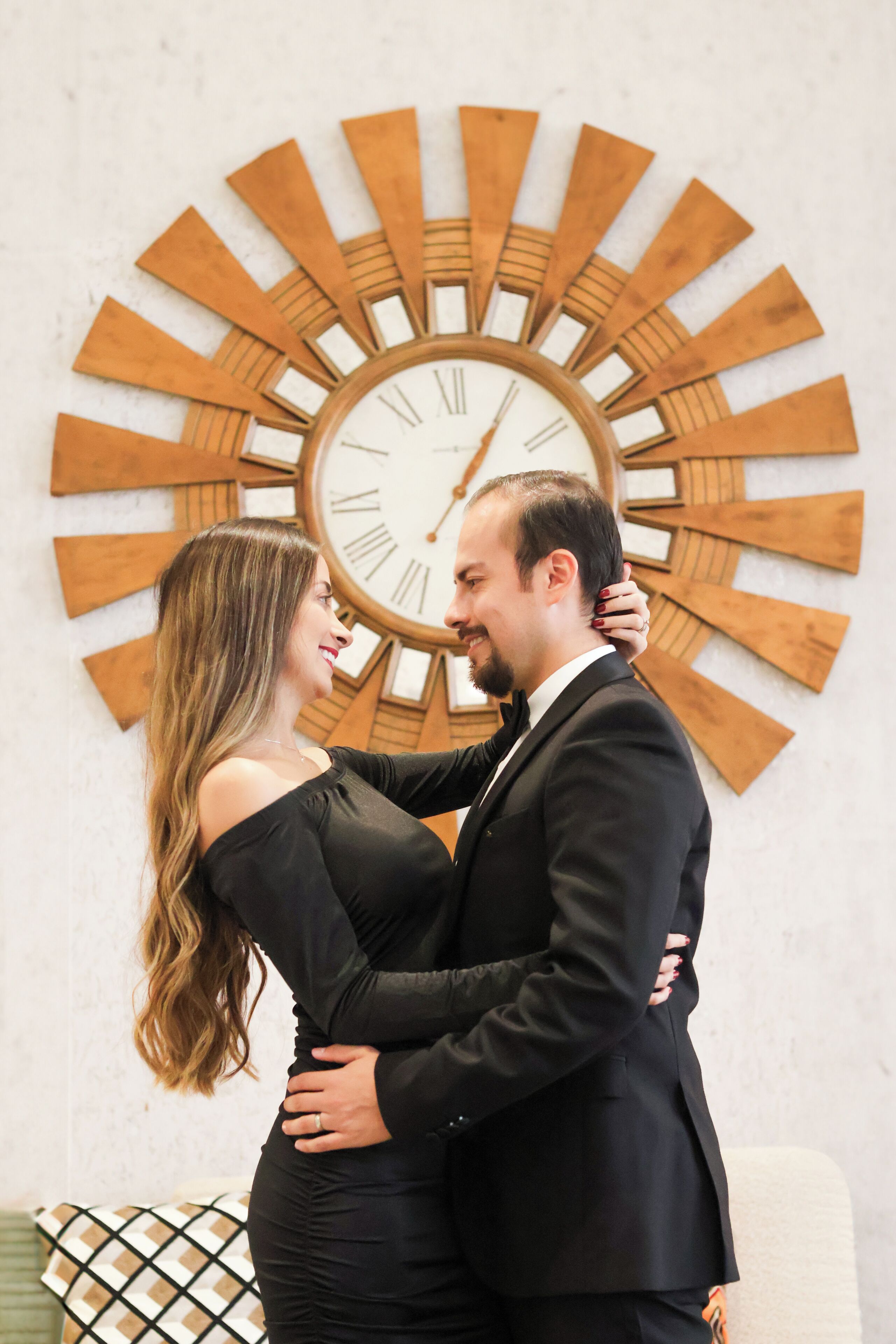 A couple embracing in front of a large wooden wall clock.