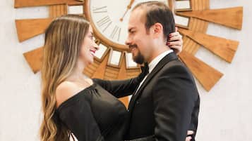 A couple embracing in front of a large wooden wall clock.