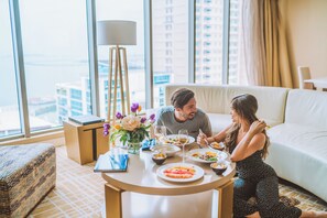 Habitación de hotel con una mesa de comedor preparada para dos personas, un sofá, una lámpara y vistas a la ciudad.