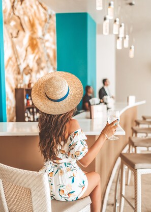 A person seated at a bar with a drink, in a room with a teal accent wall and hanging lights. - Waldorf Astoria Panama (Panama City)