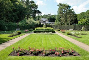 A well-manicured garden with a symmetrical layout, featuring a central hedge, flower beds, and a pathway leading to a large house. - Landgoed Hotel Het Roode Koper (Ermelo)