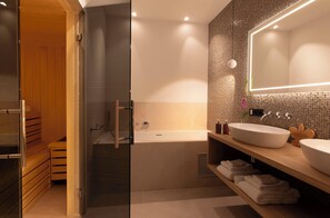 A modern bathroom with a glass shower enclosure, a freestanding bathtub, and a vanity with a large mirror and two sinks.