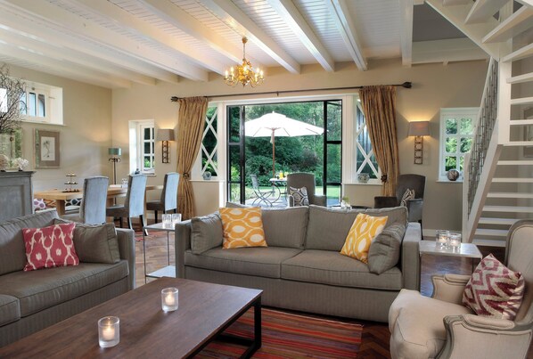 A spacious living room with a large grey sofa, a wooden coffee table, and a staircase leading to an upper level.