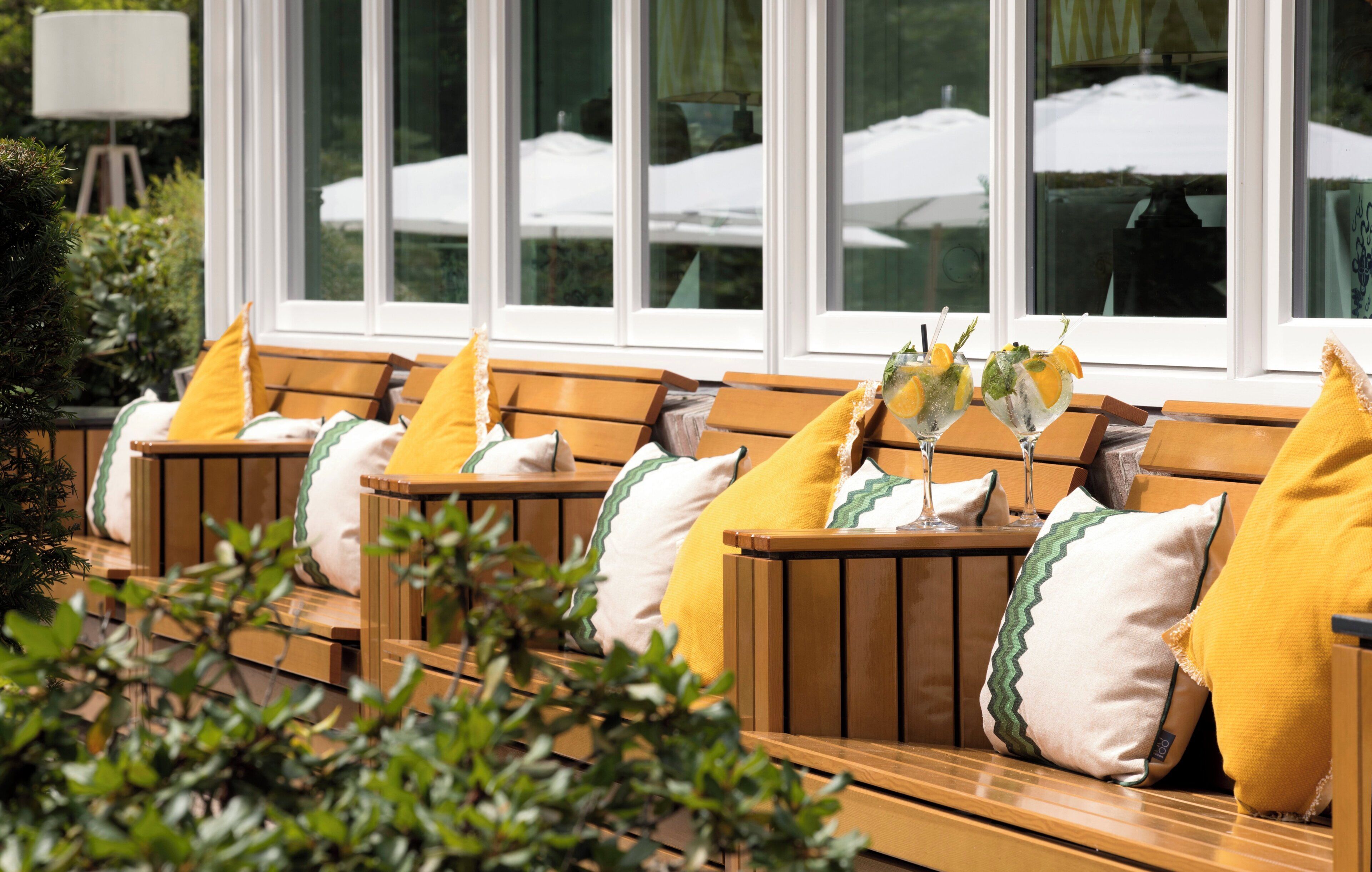 Outdoor seating with wooden benches and yellow cushions, arranged in front of a window with a view of umbrellas.