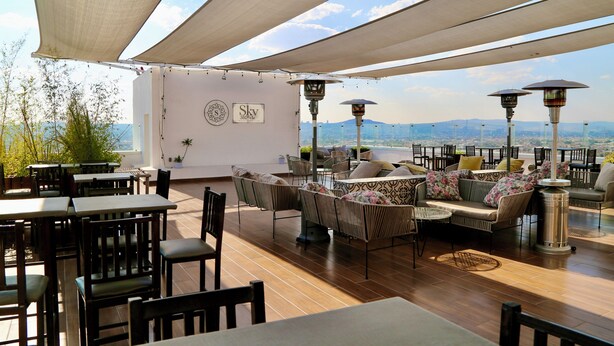 An outdoor seating area with tables and chairs, a sofa, and umbrellas. - Hotel Plaza Stadium (León)