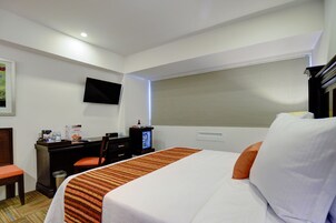 Una habitación de hotel con una cama, un escritorio con una silla, un televisor y una ventana con persianas.
