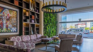 A modern lobby with a sectional sofa, armchairs, a coffee table, and a bookshelf. - Hotel Plaza Stadium (León)