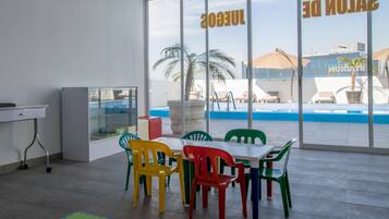 Una habitación con un ventanal grande que da a una piscina y vistas de un edificio con un letrero. Hay sillas coloridas y una mesa en la habitación.