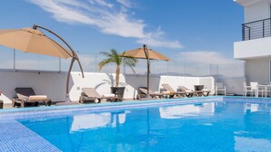 A swimming pool with lounge chairs and umbrellas, surrounded by a white building with a clear sky. - Hotel Plaza Stadium (León)