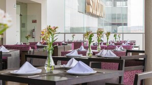 A restaurant with tables set for dining, featuring purple upholstered booths and white table settings. - Hotel Plaza Stadium (León)