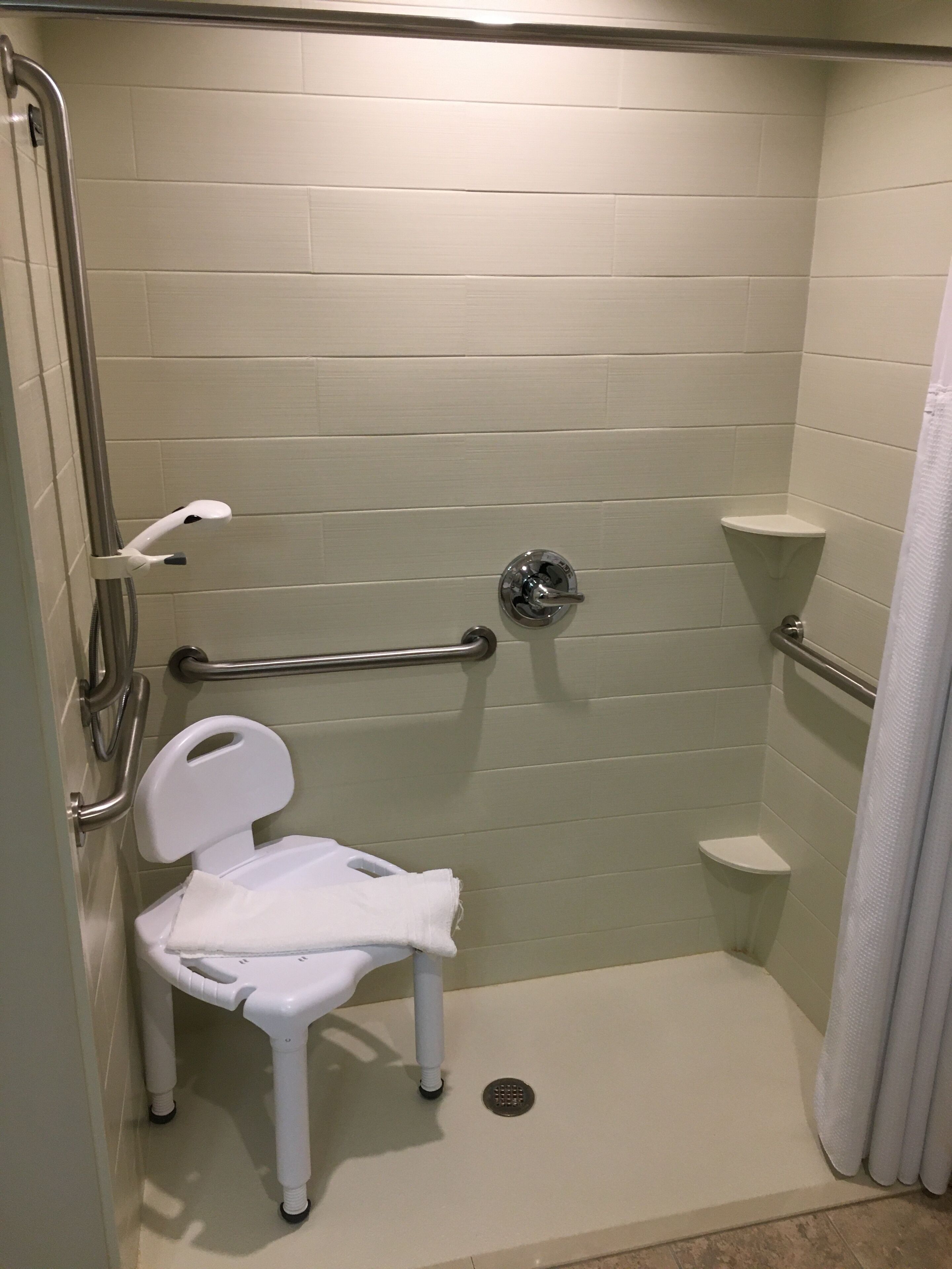 A wheelchair-accessible shower stall with a grab bar, a white toilet, and a shower seat.