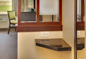 A hotel room with a wooden counter, a chair, and a mirror reflecting the room. - AmericInn by Wyndham Fairfield (Fairfield)