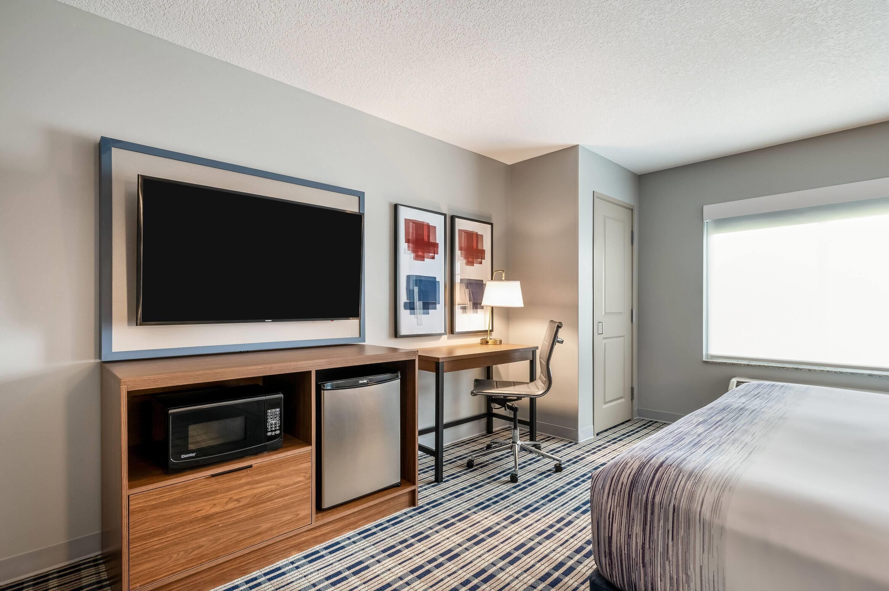 A hotel room with a bed, a desk with a lamp, a television, a microwave, and a refrigerator.