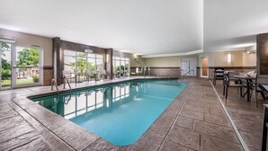 An indoor swimming pool with clear glass walls, a tiled deck, and outdoor seating. - AmericInn by Wyndham Fairfield (Fairfield)
