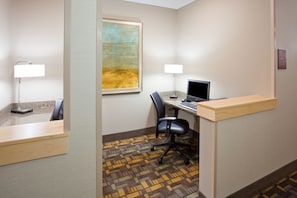 A hotel room with a desk, computer, chair, lamp, and artwork on the wall. - AmericInn by Wyndham Fairfield (Fairfield)