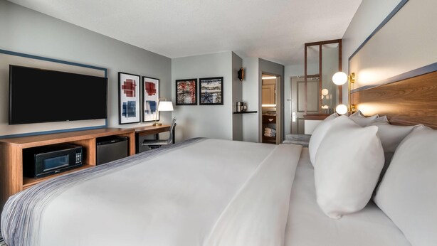 A hotel room with a bed, a desk with a microwave, a television, and artwork on the wall. - AmericInn by Wyndham Fairfield (Fairfield)