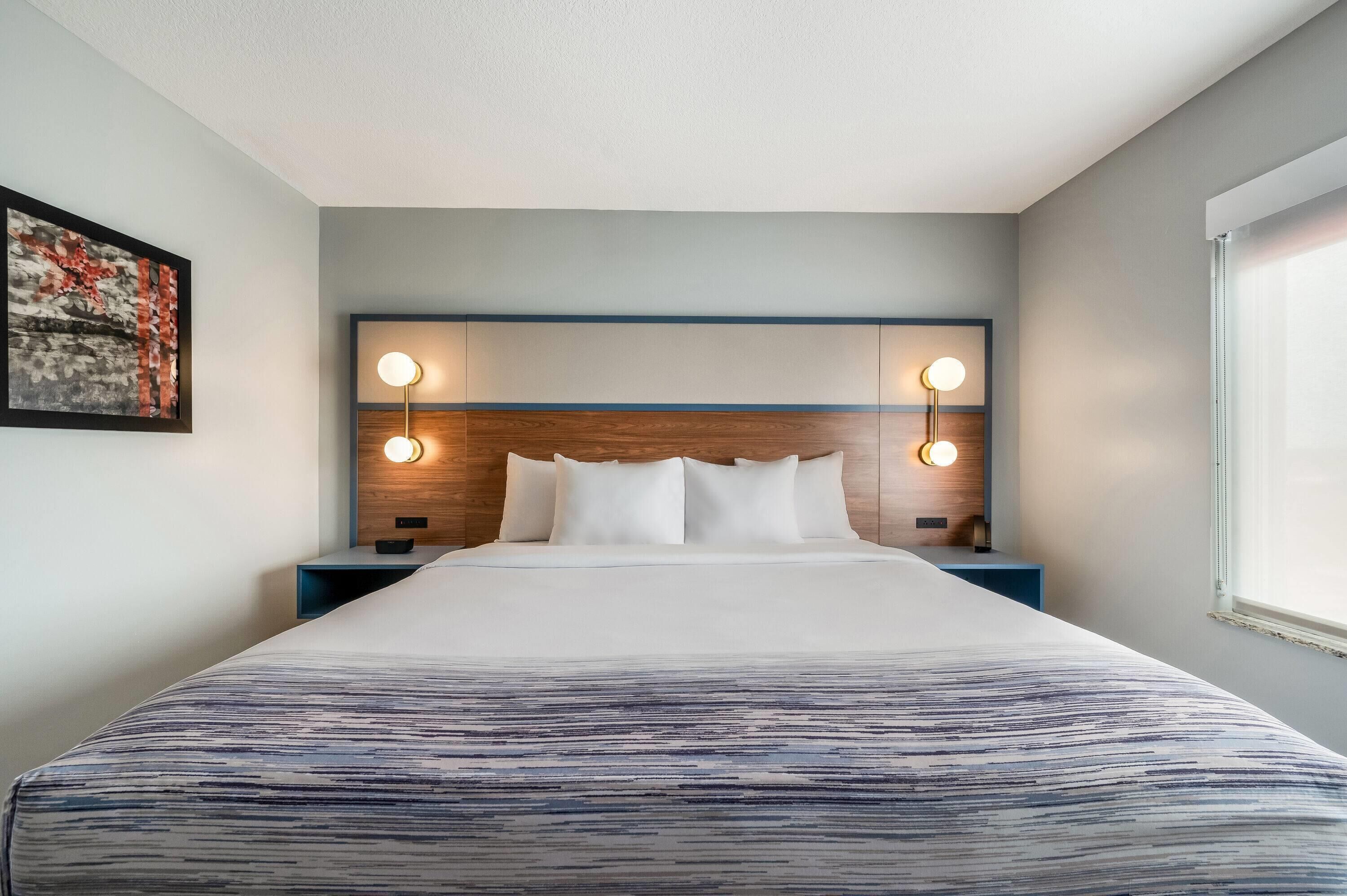 Ein Hotelzimmer mit einem großen Bett, zwei Nachttischlampen, einer Kopfteil und einem gerahmten Kunstwerk an der Wand.