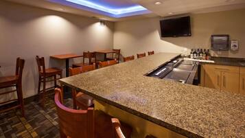 A bar area with granite countertops, wooden chairs, a flat-screen TV, and a minibar.